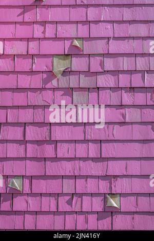 Painted peeling magenta wood shingles- San Francisco, California. Weathered painted wood shingle siding of a wall in a close-up view. Stock Photo
