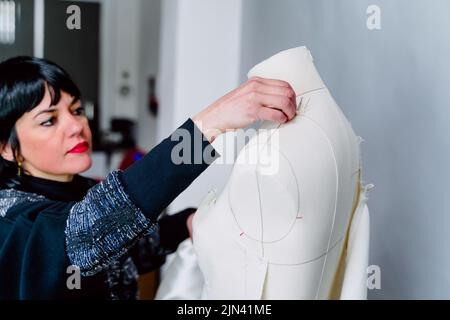 Dressmaker woman trying on the mannequin her designed clothes. Stock Photo