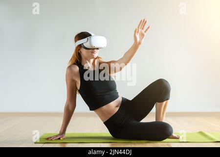 A young woman in virtual reality glasses makes fitness exercises. Future technology concept. Stock Photo