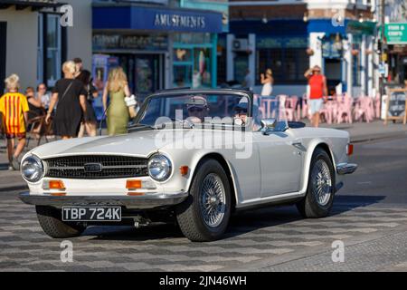 A white Triumph TR6 convertible with hood down being driven along Marine Parade on the English seaside in Essex during the heatwave of 2022 Stock Photo