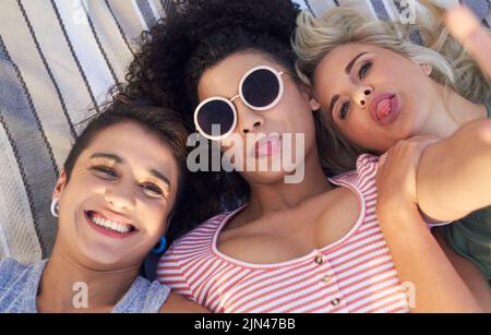 Keep your friends close and your sunglasses closer. three friends lying together on a picnic blanket. Stock Photo