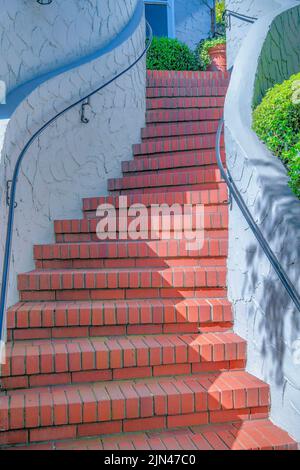 Curved staircase with bricks steps and wall-mounted handrails in San Francisco, California. Outdoor stairs with textured concrete walls leading to a b Stock Photo