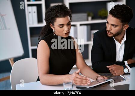 This is the best idea Ive got. two young businesspeople sitting together and having a discussion while using a tablet in the office. Stock Photo