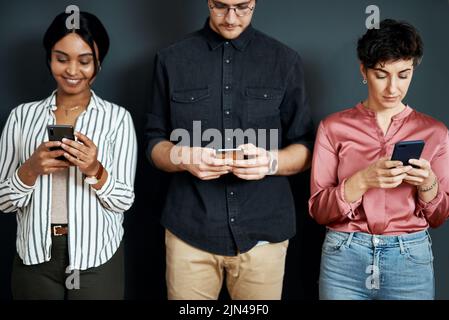 Where would millennials be without technology. a diverse group of businesspeople standing against a gray background and texting on their cellphones. Stock Photo