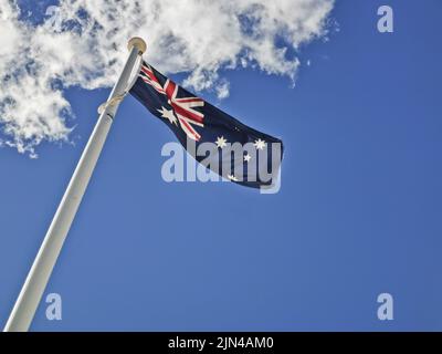 National flag of Australia consists of Union Jack and Southern Cross stars constellation in blue sky sunny day with white cloud Stock Photo