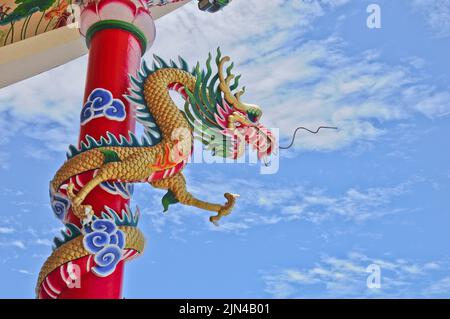 Golden flying majestic Asian Chinese dragon statue with red concrete wall and blue sky in sunny day Stock Photo