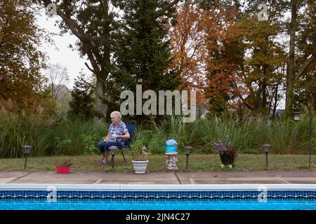 Contemplative Elderly Woman sitting in Chair near Swimming Pool Stock Photo