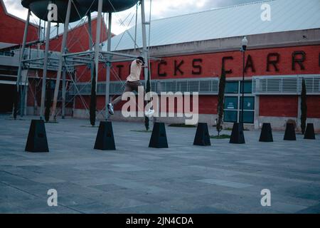 Young man dressed in a yellow shirt doing parkour. Young man dressed in urban clothes. Athlete practicing parkour on black buoys. Hispanic athlete pra Stock Photo
