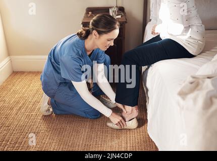 We could all use a little help in this life. a young nurse helping a senior woman get dressed in her bedroom at a nursing home. Stock Photo