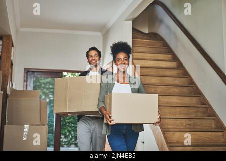 Walking into their very own space. an affectionate young couple smiling while carrying boxes into their new home. Stock Photo
