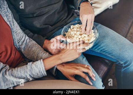 Were couch potatoes this weekend. an unrecognizable couple eating popcorn together while sitting on a sofa at home. Stock Photo