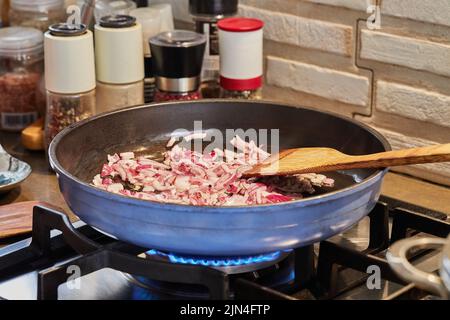 Purple onions are fried in pan on gas stove Stock Photo