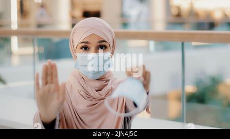 Young woman in medical protective mask shows with palm stop sign gesture forbidding to approach due to pandemic outbreak offers to put on respirator Stock Photo