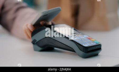 Woman at check-in desk at counter pays with smartphone through NFC contactless payment from mobile phone in bar cafe purchase of food products pay by Stock Photo