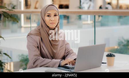 Focused serious arab businesswoman professional entrepreneur sitting at office desk typing looking at laptop screen studying online course muslim girl Stock Photo