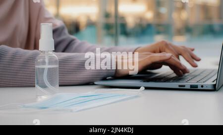 Close-up female hands young unrecognizable businesswoman typing on laptop observes precautions during pandemic takes care health uses disinfectant Stock Photo