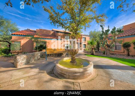 Small water fountain with garden bench near the stone walls in a residential area at Tucson, Arizona. There are mediterranean houses at the back and a Stock Photo