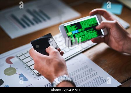 Cybersecurity issues or credit card theft by a hacker using his phone screen to write code. Closeup of the hands of man working on an interface Stock Photo
