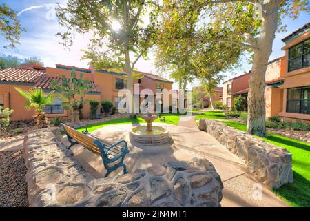 Bench near the small fountain outside the residences with italianate design exterior in Tucson, AZ. Lounge area with low stone walls near the houses w Stock Photo