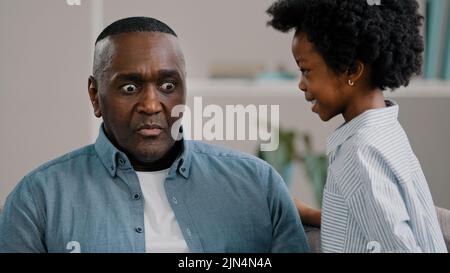 Little African American girl whispers in ear reveals secret to daddy daughter shares secrecy gossip confidential information mature father sitting on Stock Photo