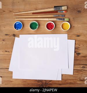 Art, painting and creative supplies on a wooden desk with paper from above. Paintbrushes, colors and still life containers ready to create artwork or Stock Photo