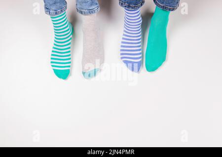 Children wearing different pair of socks. Top view to kids foots in mismatched socks sitting on white background. Odd Socks day, Anti-Bullying Week Stock Photo