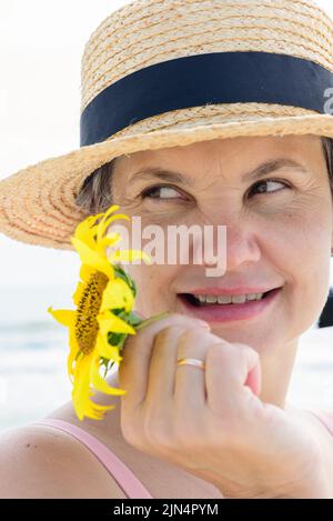 Married woman in a boater with a sunflower in her hand  playfully looking away with a little smile. Vacation concept. Stock Photo