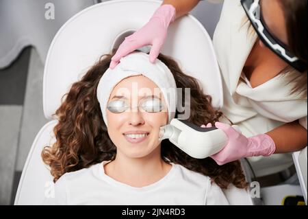 Close-up view laser correction process of vascular asterisks on face in clinic of hardware cosmetology. Doctor working with modern yellow laser for treating vascular defects of face and body. Stock Photo