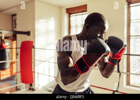 Young male boxer standing in a fighting position while wearing boxing gloves. Sporty young man having a boxing training session in a gym. Stock Photo