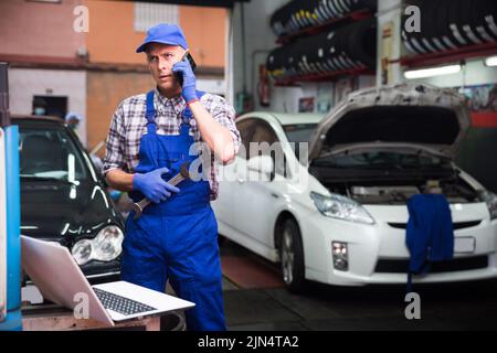 Car mechanic calls on smartphone to client Stock Photo