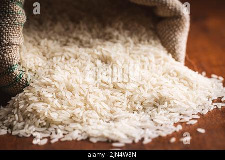 Uncooked white rice in a burlap sack on wooden table. Stock Photo