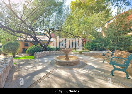 Water fountain and bench in a neighborhood at Tucson, Arizona. There are large trees on the side of walkways with lamp post near the houses at the bac Stock Photo