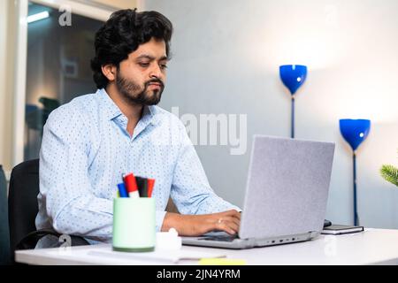 Young corporate employee or entrepreneur seriously working on laptop while sitting at office - concept of employment, hard working lifestyles and Stock Photo