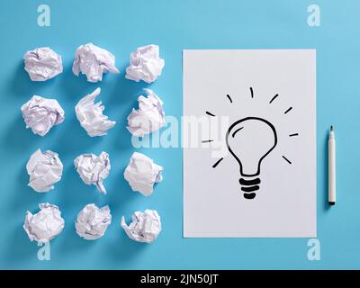 Hand drawn idea light bulb icon on a paper sheet with crumpled paper balls and a pen. Creative idea generation process concept. Stock Photo