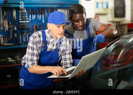 Two auto mechanics diagnosing car engine with laptop Stock Photo