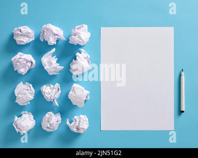 Blank white paper sheet with crumpled paper balls and a pen on blue background. Writing, brainstorming, literature, creativity and to open a new page Stock Photo