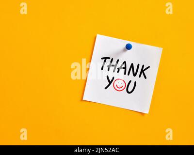 The word thank you written on a note paper pinned on a yellow board. Stock Photo
