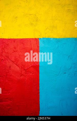 The textured wall is painted in red-turquoise and yellow bright and contrasting colors. The texture of the wall is visible through the layer of paint. Stock Photo