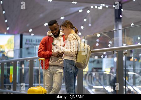 Young multiracial couple in airport looking at map in smartphone, booking hotel or accommodation Stock Photo