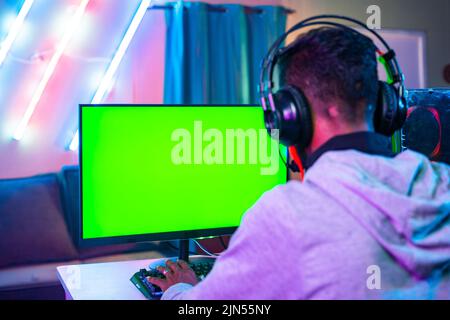 shoulder shot of professional gamer playing live video game on green screen monitor by talkng on headphones - concept of entertainment, excitement and Stock Photo