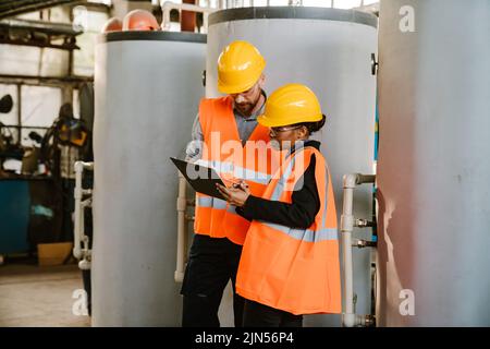 Multiracial man and woman in protective clothing working together at factory Stock Photo