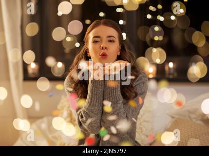 woman blowing confetti from her hands at night Stock Photo