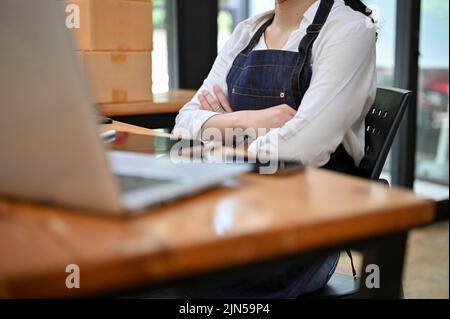 A professional young Asian female entrepreneur or small online business owner sits at her office desk with arms crossed. cropped image Stock Photo