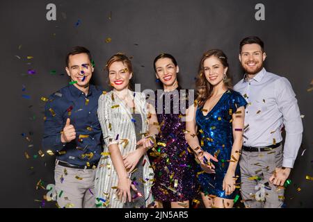 happy friends at party under confetti over black Stock Photo