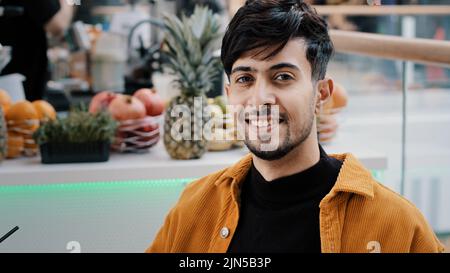 Young hispanic male cafe client resting spending weekend drinking exotic drink from plastic disposable cup relaxing happy carefree guy enjoying taste Stock Photo
