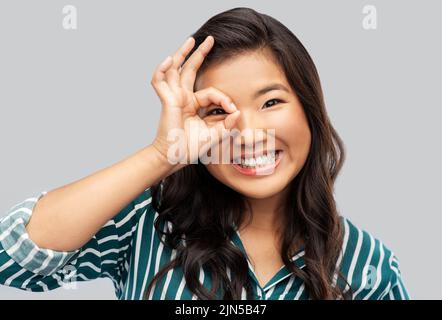 smiling asian woman looking through finger glasses Stock Photo