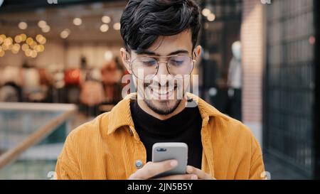 Close-up happy indian guy laughs watching funny video on smartphone looking at phone screen browsing web page on social network young man typing sms Stock Photo