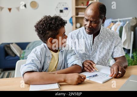 Schoolboy having lesson with tutor, they sitting at desk in the room and doing homework together Stock Photo