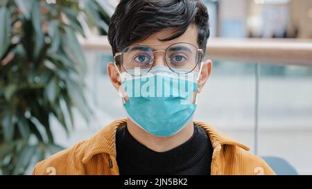 Portrait close-up young indian guy in protective medical mask standing indoors confident man posing looking at camera personal safety due pandemic Stock Photo