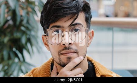 Headshot young pensive thoughtful indian man holding hand on chin thinking deep in thought in search decides finds solution to problem difficult Stock Photo